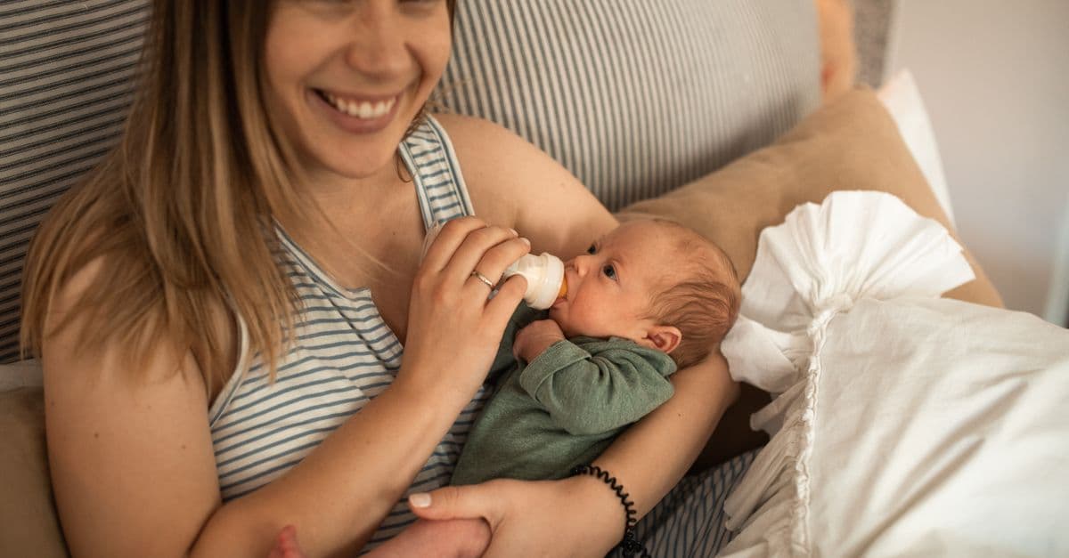 A smiling parent feeding their newborn baby
