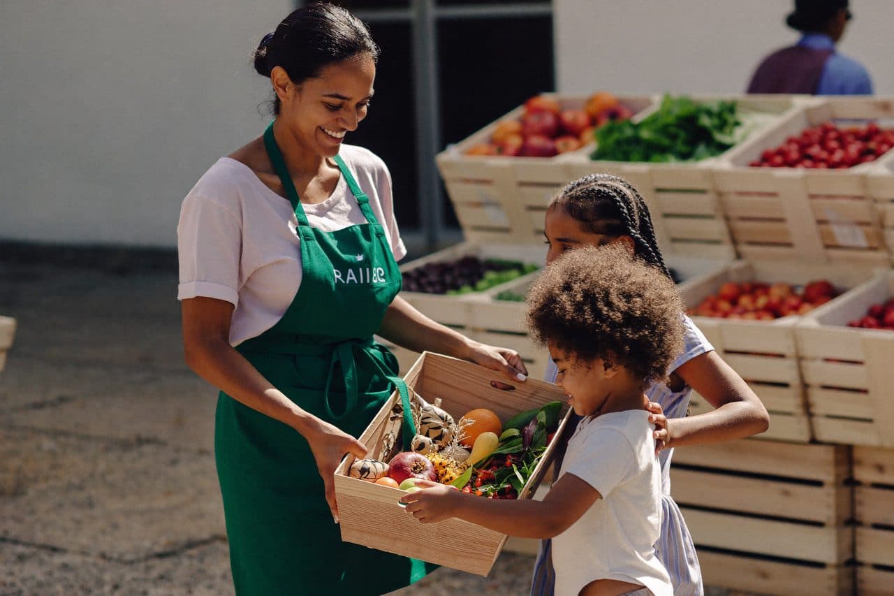 A volunteer handing a basket of fresh produce to a family
